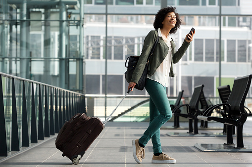 Full body side portrait of travel woman walking at station with suitcase and  cellphone