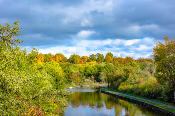 Autumn nature.Trees with leaves changing colour reflect in calm water of Trent and Mersey canal in central England. Landscape of England.Trent and Mersey canal in Stoke on Trent, Staffordshire,Uk on beautiful autumn day.Trees with leaves changing color and cloudy sky in background reflecting in water. stoke on trent stock pictures, royalty-free photos & images