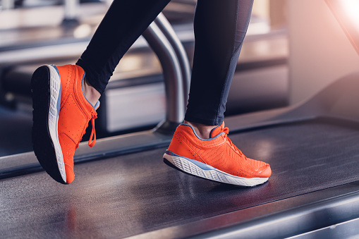 Comfortable sports shoes for running in the gym. Jogging shoes for running on a treadmill. Safety when performing exercises on cardio in sports shoes. Orange sports sneakers on the treadmill