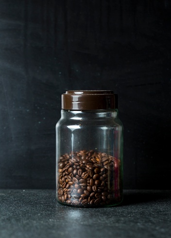 Glass jar with coffee beans on dark background. Close up of coffee.