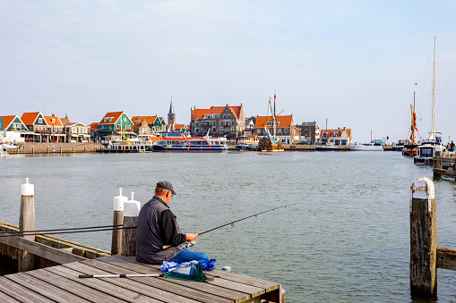 Volendam, Netherlands - September 3, 2018: A fisherman enjoy some quiet fishing at the popular harbour in Volendam, one of North Holland's most popular tourist destinations.