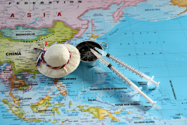 A compass with two disposable syringes and travel cap on world map. stock photo