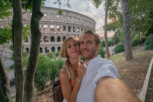 Selfie portrait of young couple in Rome enjoying travel in Italy and capturing  a photo in front of the famous Colosseum; People travel capital in Europe concept