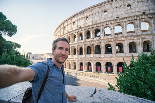 Selfie portrait of young man in Rome enjoying travel in Italy and capturing  a photo in front of the famous Colosseum; People travel capital in Europe concept