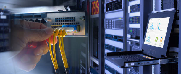 engineer and fiber optic cable on network router switch and monitor show graph information in background in technology data center room. widescreen stock photo