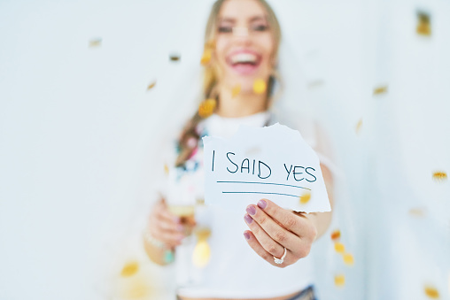 Shot of a young woman holding a paper with the words “I said yes” announcing her engagement
