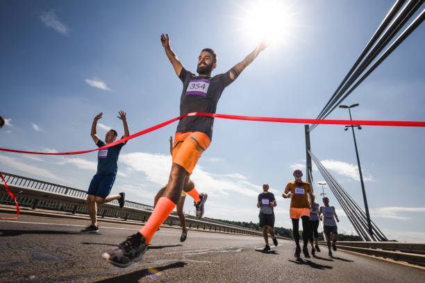 vista de ángulo bajo de exitoso hombre cruzando la línea de meta en raza del maratón. - finish line fotografías e imágenes de stock