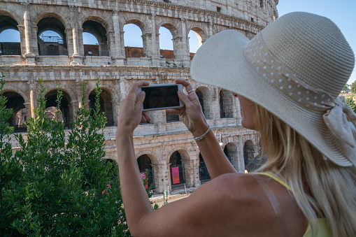 Young woman in Rome enjoying travel in Italy and capturing a photo of the Trevi fountain using her smart phone ; People travel capital in Europe concept