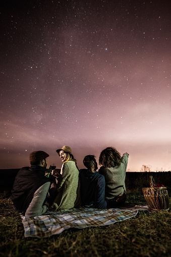 Two romantic couples enjoying on picnic in a meadow under starry sky at night. Copy space.