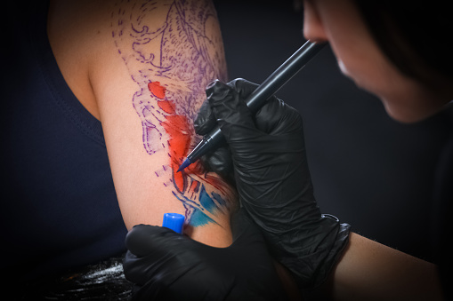Female tattoo artist making tattoo on a men`s arm