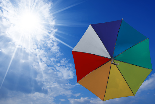 Multicolor umbrella flying in a blue sky with clouds and sun rays