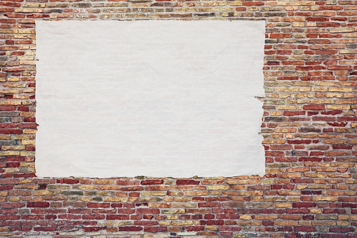 blank advertising poster glued to the brick wall - copy space in street billboard