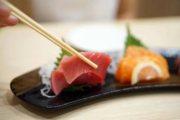 Photo of Hand holding chopsticks to pick chutoro sashimi and dip into soy sauce.