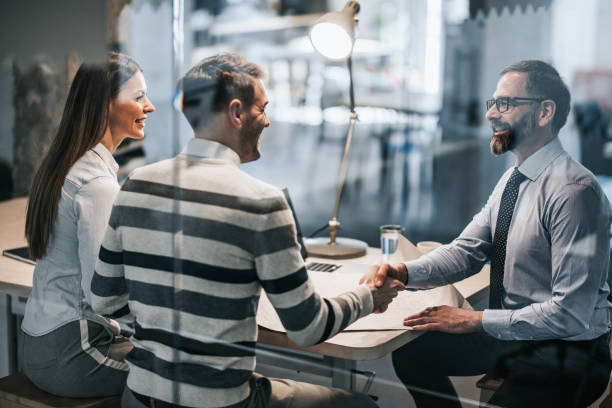 Happy couple shaking hands with real estate agent in the office. Happy real estate agent shaking hands with young couple after successful meeting in the office. The view is through glass. customer stock pictures, royalty-free photos & images