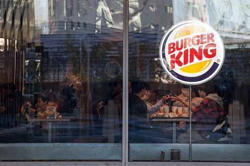 Picture of a Burger King sign on their restaurant in Montreal, Quebec, Canada, with clients eating hamburger in the background. Burger King is an American global chain of hamburger fast food restaurants