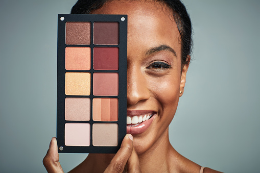 Studio shot of a beautiful young woman holding a make up palette against a grey background