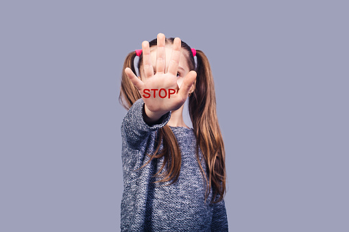 sad little girl shows hand stop sign. Concept stop child  . isolated on gray background