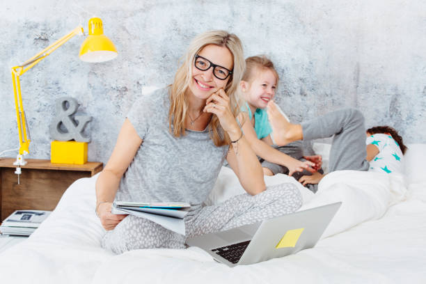 happy business mum at work while her kids are playing in bed and having fun - proof of love imagens e fotografias de stock