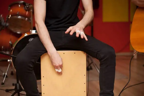 Photo of Percussionist playing cajon on a rehearsal studio with drums and music stuff on the background