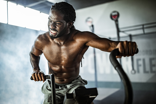 African American athletic man making an effort while being on exercise bike in a gym.