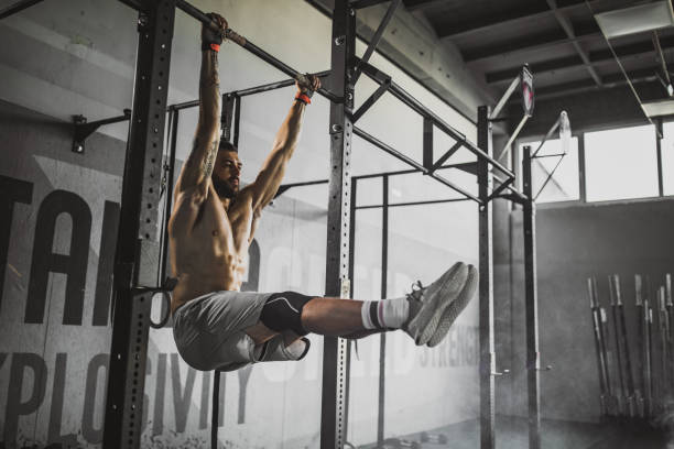 Young muscular build athlete exercising strength in a gym. Muscular build male athlete exercising chin-ups during cross training in a gym. chin ups photos stock pictures, royalty-free photos & images