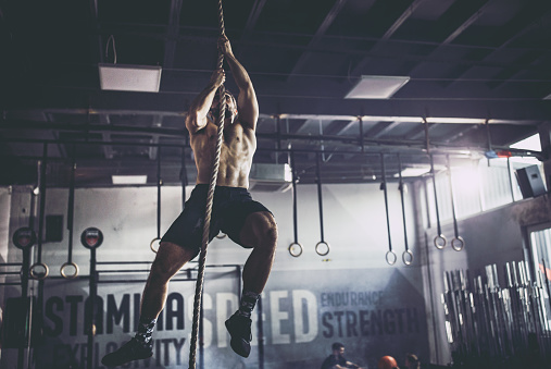 Deportista musculoso trepando por la cuerda en un gimnasio. photo