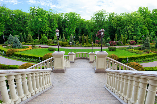 Stylish granite staircase with a balustrade with beautiful carved balusters in classic style, overlooks the beautiful lawn of a magnificent garden.