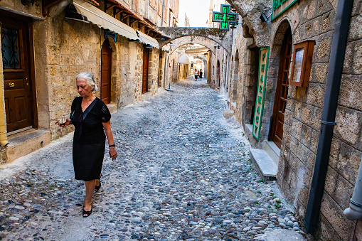 Rhodes, Greece - 21 June , 2009: An elegant Greek old lady walking through the narrow streets of Rhodes holding two pieces of bread