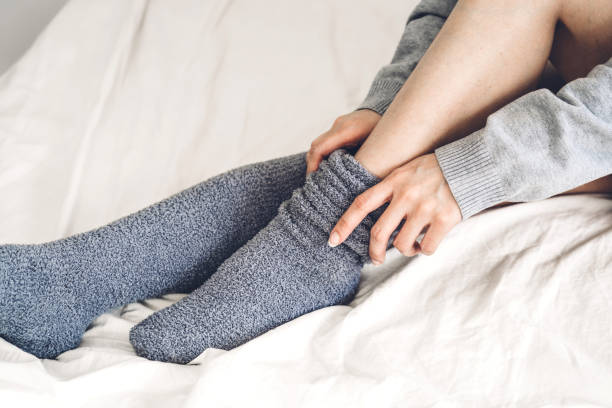 Woman sit on the bed wearing and putting on long warm socks in cold winter day stock photo