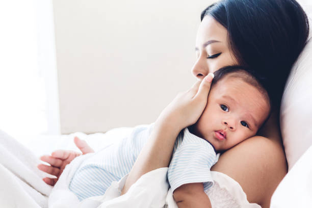 mãe de bebê segurando em seus braços e beijar em um quarto branco. amor do conceito de família - new mother - fotografias e filmes do acervo