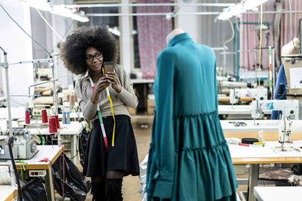 Female designer with tape measure using phone Female designer with tape measure working in fashion studio. clothing design studio stock pictures, royalty-free photos & images