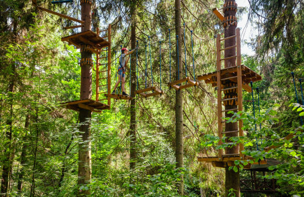 teen boy sur un parcours d’accrobranche en hauteur dans un passage de parc aventure treetop suspendus obstacle de corde - high up obstacle course ropes course teenage boys photos et images de collection