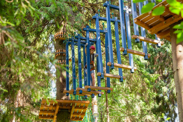 teen boy sur un parcours d’accrobranche en hauteur dans un passage de parc aventure treetop suspendus obstacle de corde - high up obstacle course ropes course teenage boys photos et images de collection