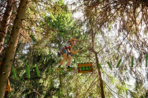 ragazzo adolescente su un corso di corde in un parco avventura sugli alberi passando un ostacolo di corda appesa - high up obstacle course ropes course teenage boys foto e immagini stock