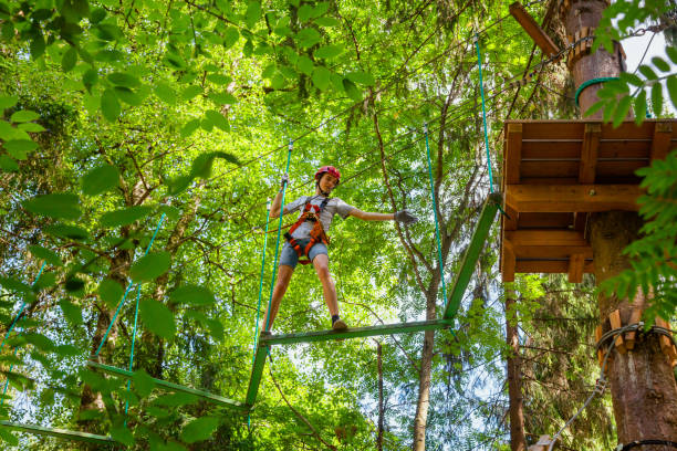 Teen boy on a ropes course in a treetop adventure park passing hanging rope obstacle stock photo