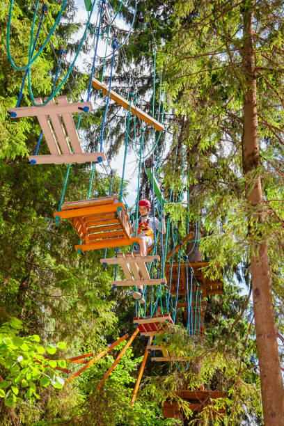 teen boy sur un parcours d’accrobranche en hauteur dans un passage de parc aventure treetop suspendus obstacle de corde - high up obstacle course ropes course teenage boys photos et images de collection