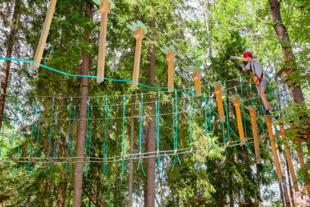 teen boy sur un parcours d’accrobranche en hauteur dans un passage de parc aventure treetop suspendus obstacle de corde - high up obstacle course ropes course teenage boys photos et images de collection