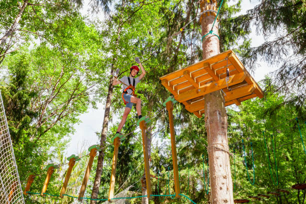 ragazzo adolescente su un corso di corde in un parco avventura sugli alberi passando un ostacolo di corda appesa - high up obstacle course ropes course teenage boys foto e immagini stock