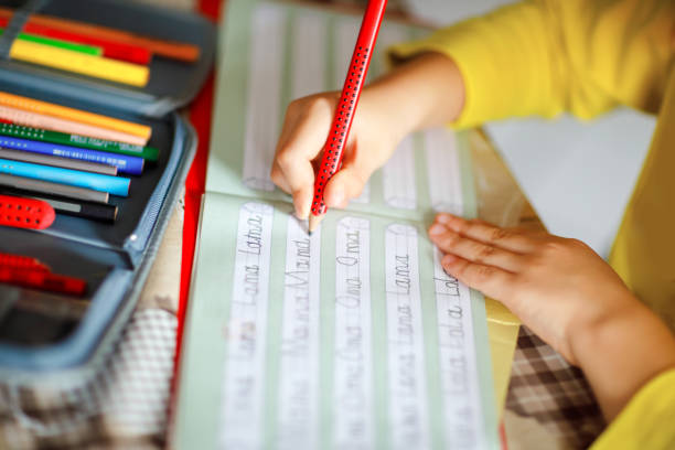 close-up of little kid boy at home making homework, child writing first letters and words like mama with colorful pens. Elementary school and education stock photo