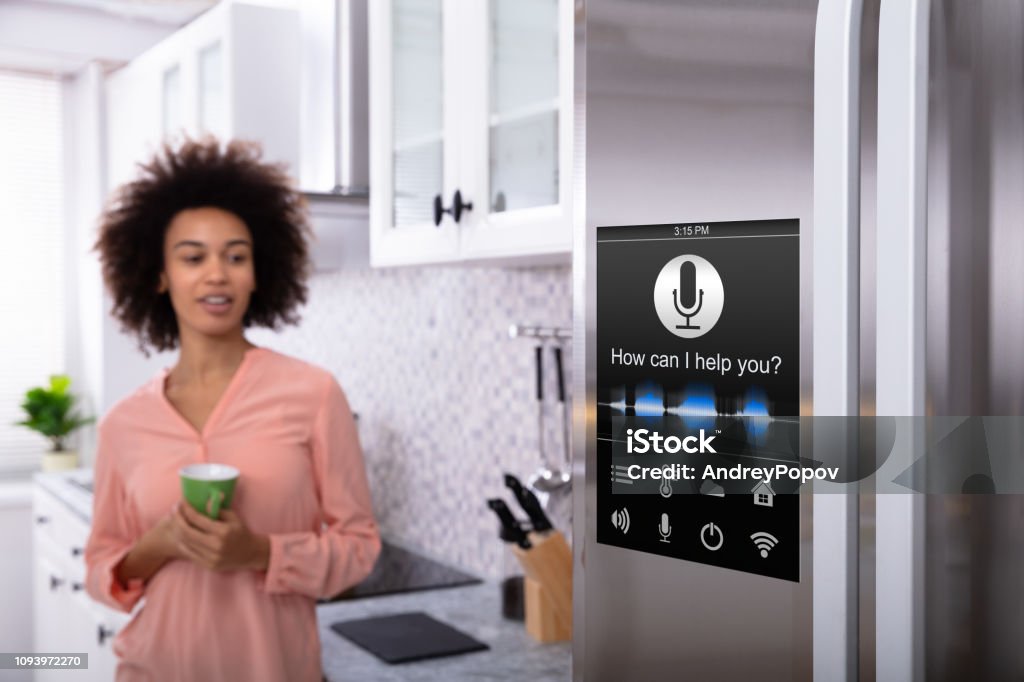 Woman Standing Near The Refrigerator With Voice Recognition Young Woman Holding Green Coffee In Hand Looking At Refrigerator With Voice Recognition Function Refrigerator Stock Photo