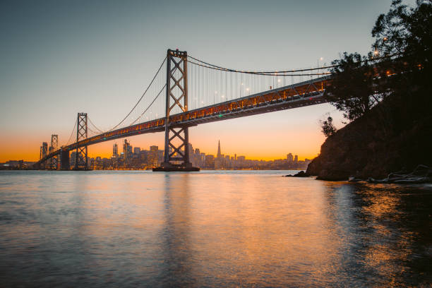 skyline de san francisco con oakland bay bridge en la puesta del sol, california, eeuu - golden gate bridge night bridge san francisco bay fotografías e imágenes de stock