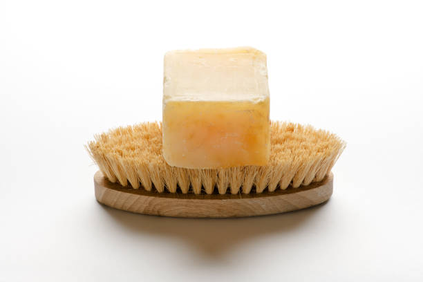 Piece of Marseille soap, made of vegetable oil, sitting on bathing brush, isolated on white background with shadow
