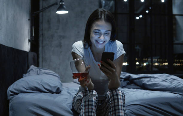 social viciado em mulher jovem e bonita olhando para smartphone, usando o app de namoro on-line, bebendo vinho, sentado na cama à noite - internet dating dating togetherness internet - fotografias e filmes do acervo