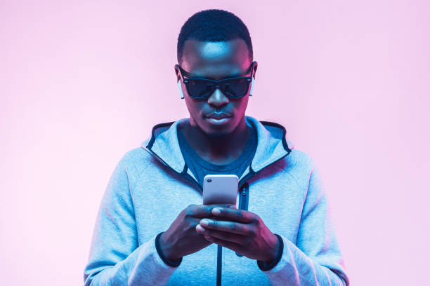istock Young black male looking at smartphone while texting his friend, using mobile phone, isolated on pink background 1093991936