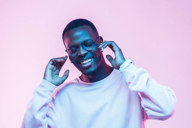 joven guapo hombre africano en auriculares inalámbricos y escuchar su canción favorita, bailando, sonriendo con los ojos cerrados - contemporary style audio fotografías e imágenes de stock