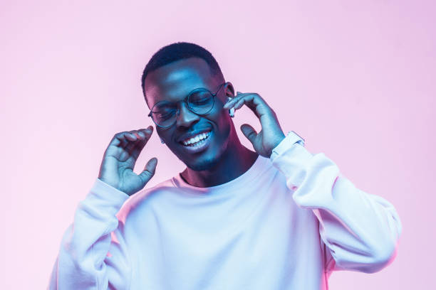 jeune bel homme africain en casque d’écoute sans fil et en écoutant sa chanson préférée, danser, sourire avec les yeux fermés - expressive hands audio photos et images de collection