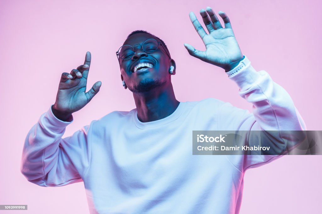 Young african man listening to music with wireless earphones and dancing isolated on pink background Dancing Stock Photo