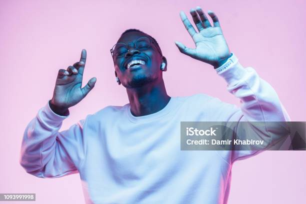 Young African Man Listening To Music With Wireless Earphones And Dancing Isolated On Pink Background Stock Photo - Download Image Now