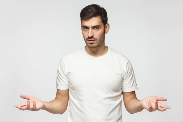 Young man spreading hands not knowing what to do, isolated on gray background