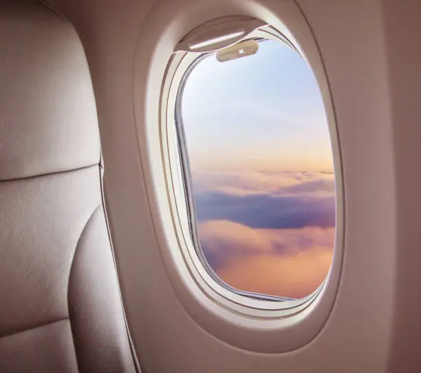 Airplane interior with window view of sunset above clouds. Concept of travel and air transportation